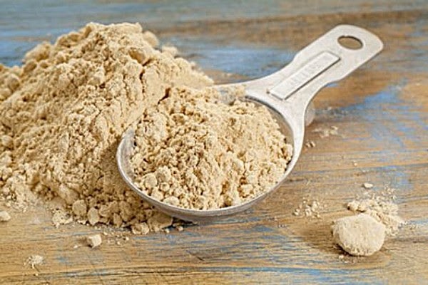 Organic protein powder in a metal scoop on a wooden surface.