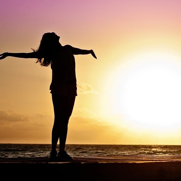 Sunset beach scene with a woman standing with arms open during a vibrant sunset.